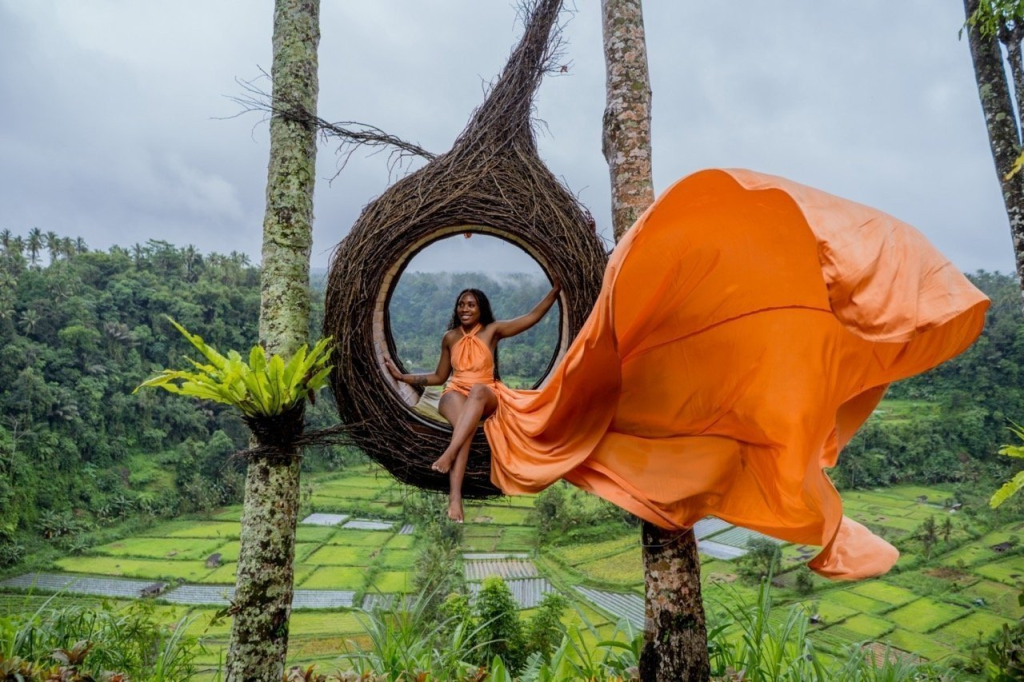 A woman in an orange dress posing in a cocoon swing in Bali