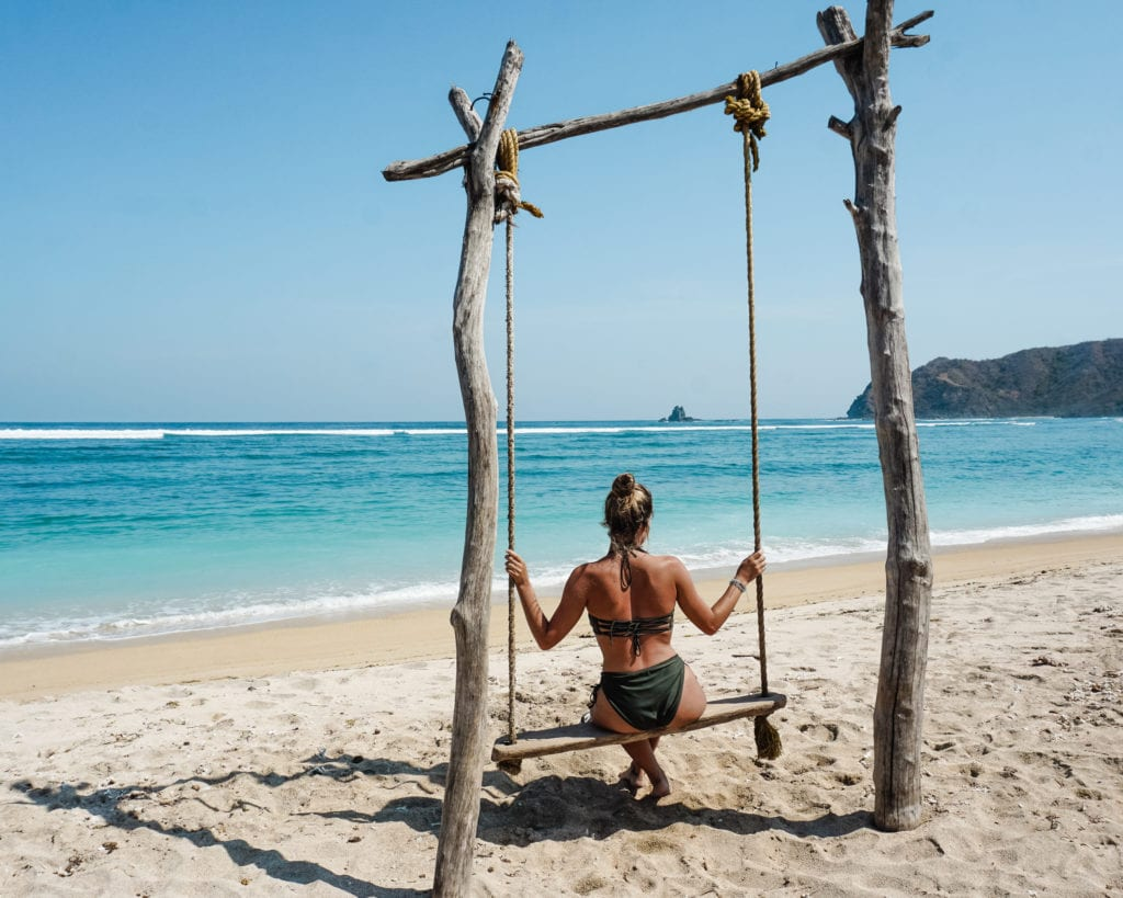A woman sitting on a rope swing on a deserted beach