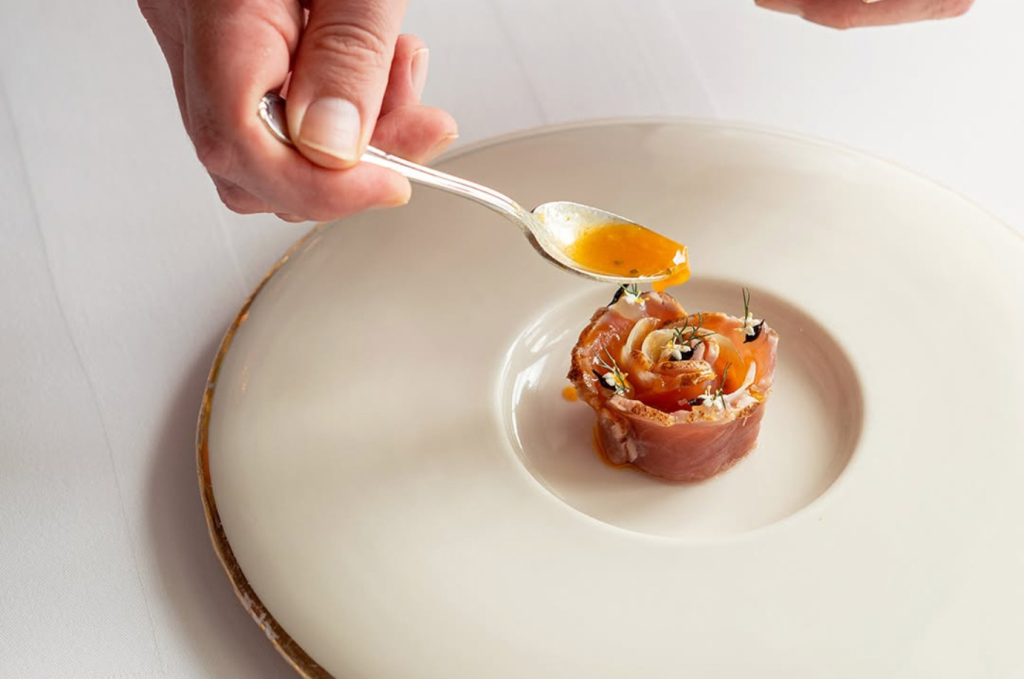 A fine dining meal of cured ham elegantly displayed with a sauce drizzled on top
