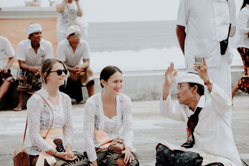 A local Balinese person explaining Bali languages to two tourists wearing traditional clothing
