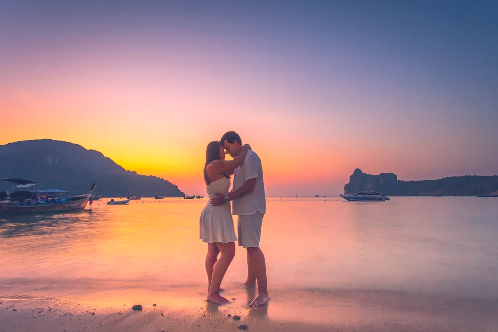 A couple embracing each other on a beach on their honeymoon with a sunset in the background
