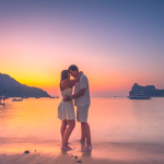 A couple embracing each other on a beach on their honeymoon with a sunset in the background