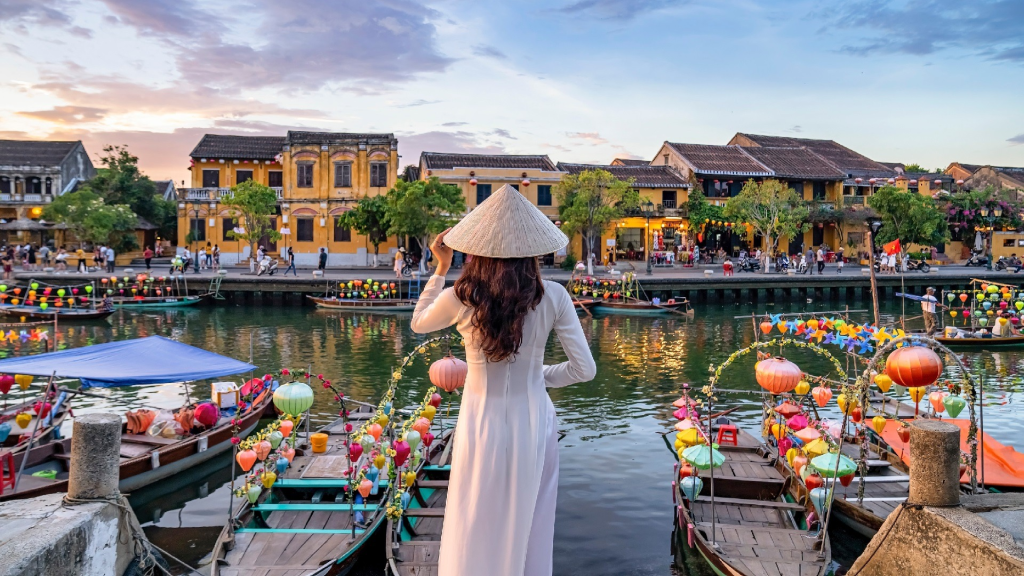 A woman standing by colourful small boats by the river in Hoi An, Vietnam