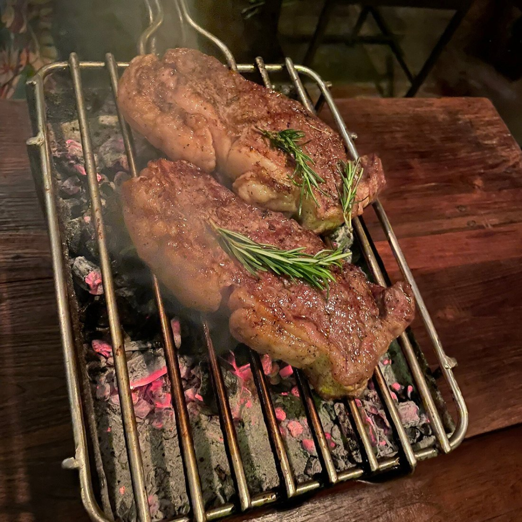Two steaks on a grill with rosemary garnish