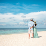 A couple standing on a pristine beach looking out to the ocean on their honeymoon